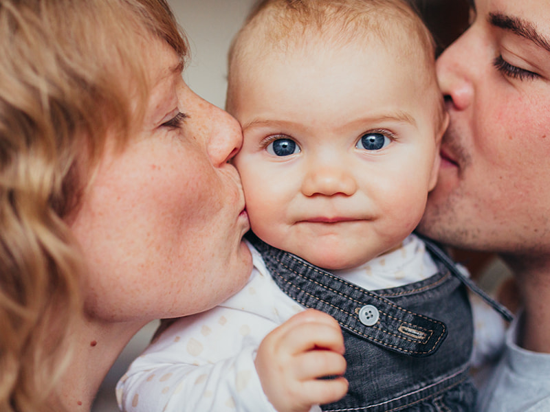Mother and father kissing their child on each cheek simultaneously